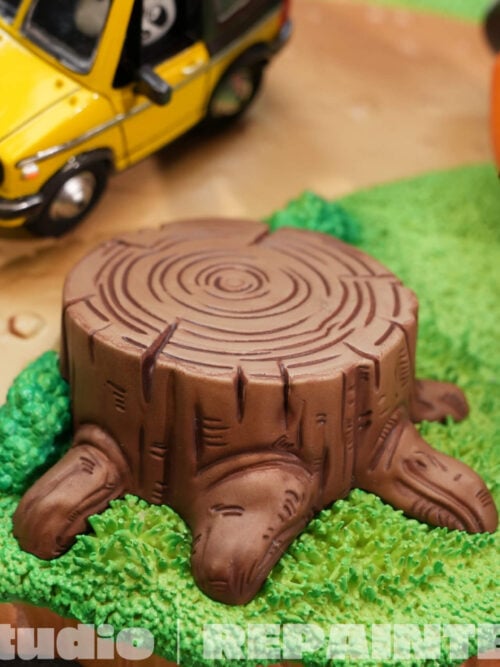 Close-up of the sculpted tree stump and textured grass, with the yellow car and part of Goku's staff carrier behind it.