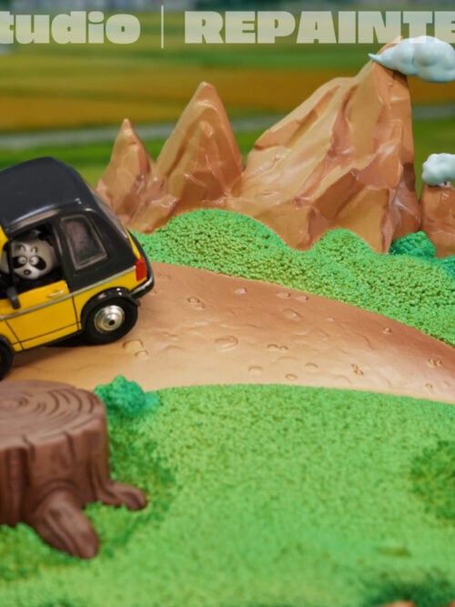 Scenic base shown without Goku, featuring a yellow car, dirt path, tree stump, rock and mountain peaks with small clouds.