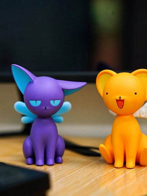 Purple Spinel Sun and yellow Keroberos figures seated side by side on a desk, with blue and white wings respectively.