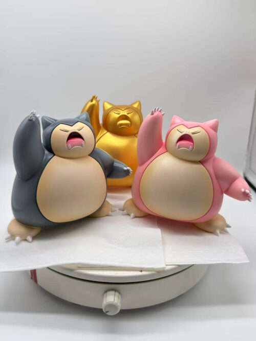 Dark gray and pink Snorlax figures in front of a gold figure, shown together on a turntable for color comparison.