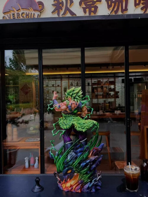 Full view of green-haired Broly on a café table, with a raised hand, flowing green waist pelt and rocky dragon-head base.