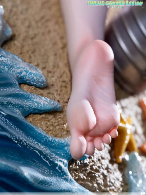 Vertical close-up of the Gouden Leeuw statue's bare foot beside textured sand and sculpted blue surf.