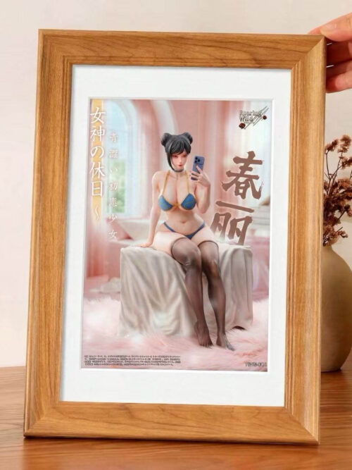 A hand holds a wood-framed print of the seated Chun-Li statue on a table beside a pinecone, dried flowers, and a candle.