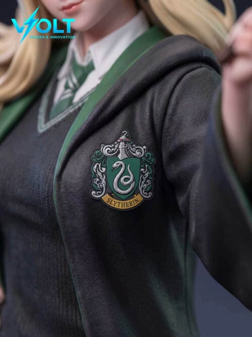 Close-up of the dark robe chest showing a green-and-silver crest with a snake and a banner reading SLYTHERIN, next to a white collar and green striped tie.