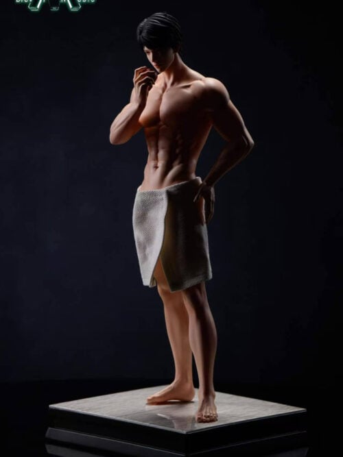Three-quarter view of the shirtless Caleb statue in a white bath towel, looking down at a red apple held near his mouth, with one hand at his hip. He stands barefoot on a gray tiled base against a dark background.
