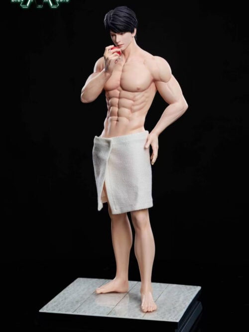 Frontal view of the shirtless Caleb statue with black hair and a white bath towel, holding a red apple near his mouth and resting one hand at his hip. He stands barefoot on a gray tiled base with a black platform.