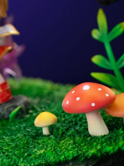 Close-up of the grassy terrain base on Time Studio's Evan & Mir MapleStory statue highlighting a red white-spotted mushroom, an orange mushroom, a small yellow mushroom, and a green leafy stem.