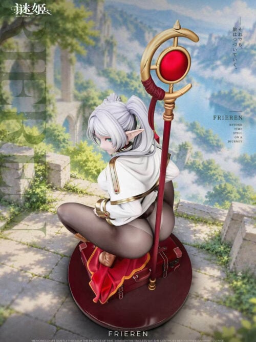 Rear three-quarter promotional view of the same Frieren figure crouching over stacked red suitcases on a round dark-red base. The silver-white hair, pointed ear, white coat with gold edging, brown leggings and the tall staff with a gold crescent and red orb are visible against a tree-lined path and distant landscape, with MiJi Studio branding.