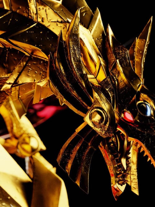 Close-up of The Winged Dragon of Ra's textured metallic gold head and neck armor with a blue forehead orb, glowing red eye, and open toothed beak