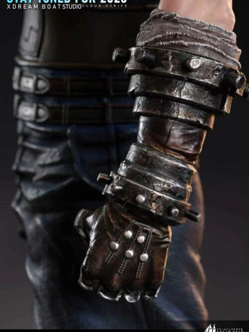 Close-up of Cloud Strife statue left arm showing the weathered bolted metal gauntlet, leather bracer, and studded glove