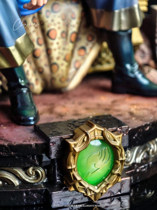 Close-up of the gold-framed green Fairy Tail emblem on the front of the base with Natsu's boots and leopard-print drapery behind