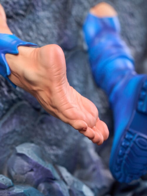 Close-up of the lower rear of the statue, showing a bare sculpted foot and a blue boot sole with visible tread emerging from the gray rocky base.