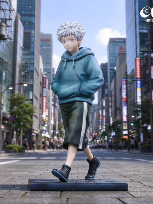 GUGU Studio and MIMO Studio Young Satoru Gojo 1/6 figure walking with hands in the pocket of a blue hoodie and dark shorts on a rectangular base against a city street backdrop.