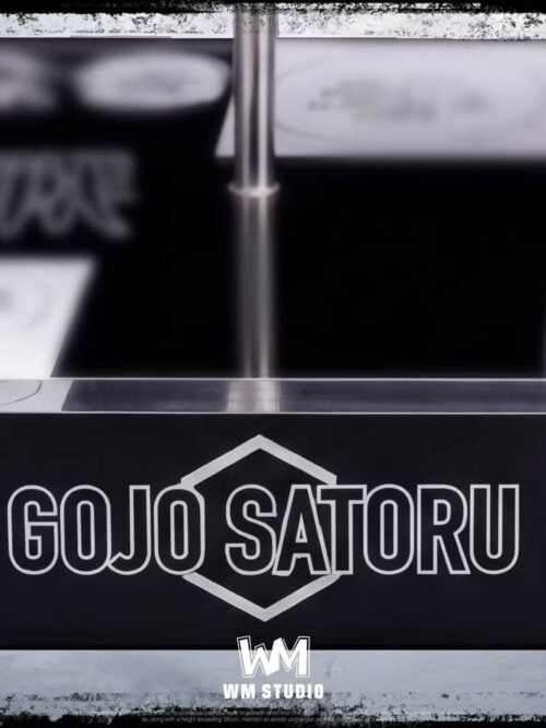 Close-up view of the rectangular black display base front featuring the white GOJO SATORU emblem, metal support rod, and manga panels beneath a clear surface.